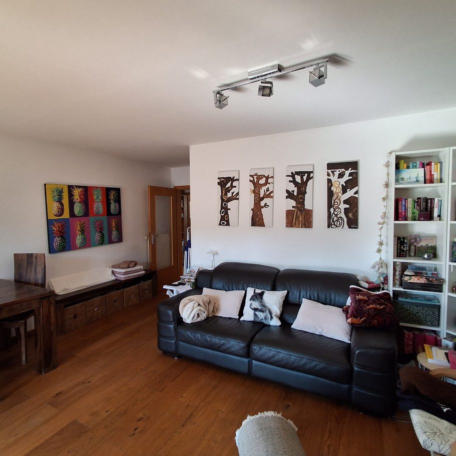 Wohn- und Esszimmer Moderne Wohnzimmer mit schwarzem Sofa, Bücherregal und bunten Wandbildern.