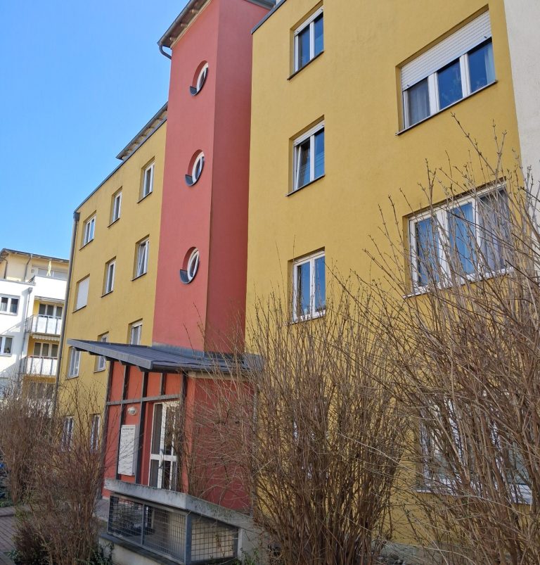 Hauseingang Buntes Wohngebäude mit gelber und roter Fassade und runden Fenstern.